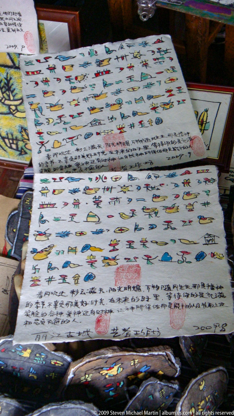 Handwritten dongba-style sheet from Lijiang, China, showing Chinese text with colorful pictographs of humans, animals, and objects, plus a red seal stamp and date-like notation at the bottom.