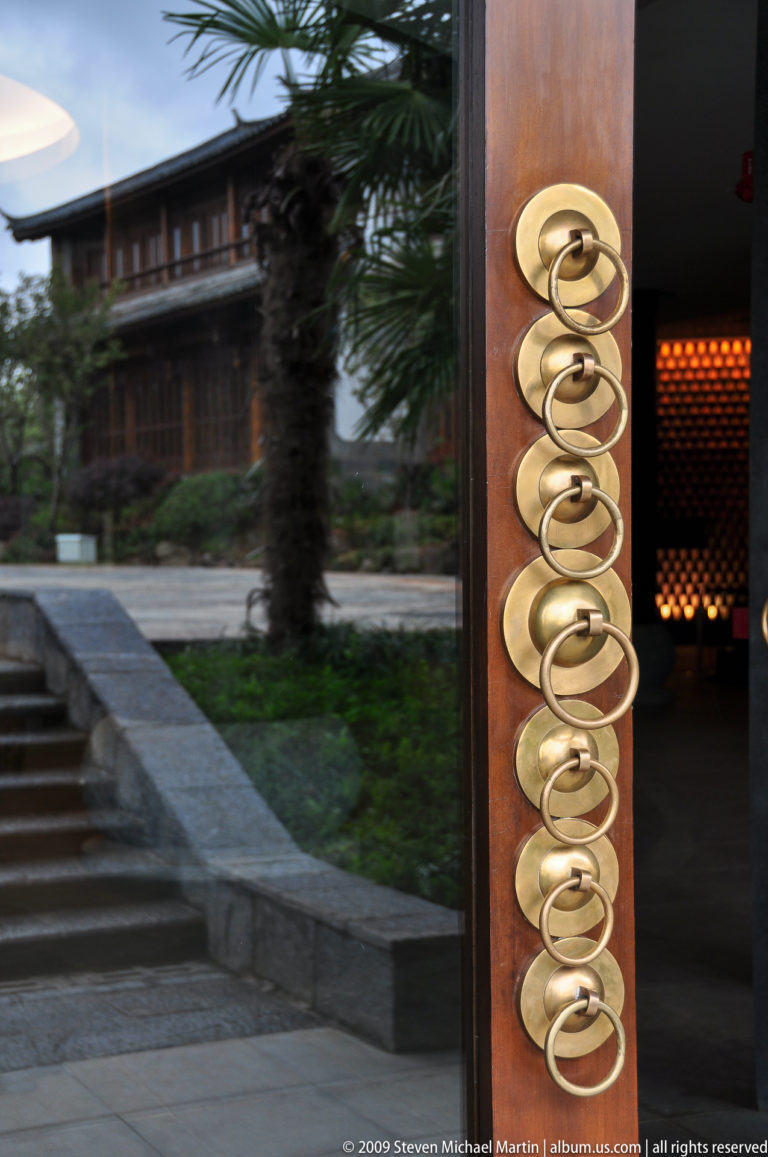 Close-up of five brass ring pulls mounted on a wooden frame next to reflective glass and a patterned illuminated wall.