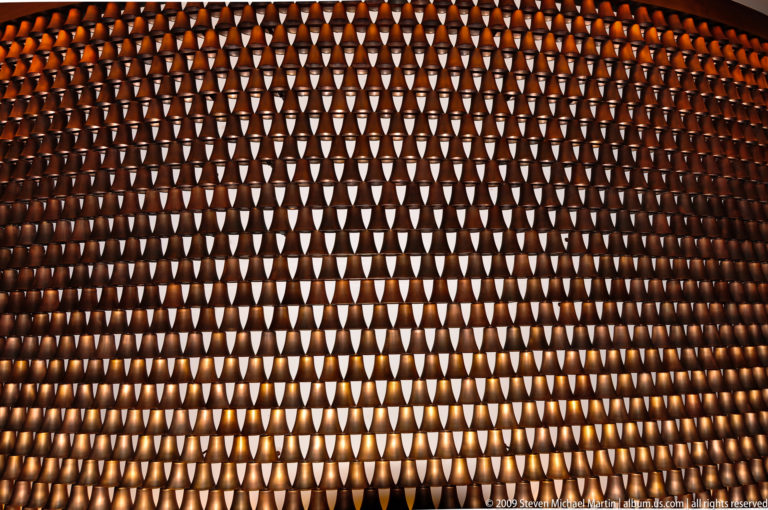 Backlit interior wall in Lijiang, China, made of repeated bronze cup-like modules arranged in a glowing geometric grid.