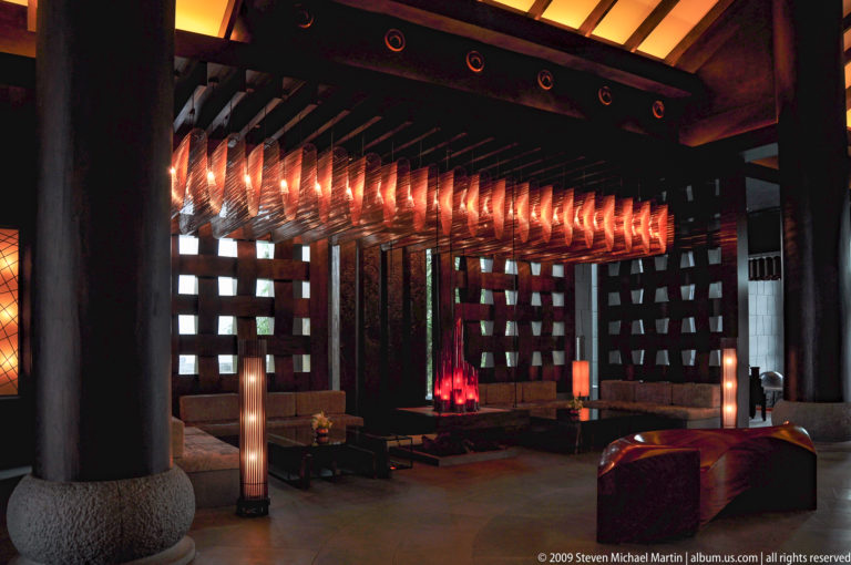Modern lounge interior in Lijiang, China, with hanging sculptural lights beneath black ceiling beams and surrounded by wood lattice screens, columns, and low tables.