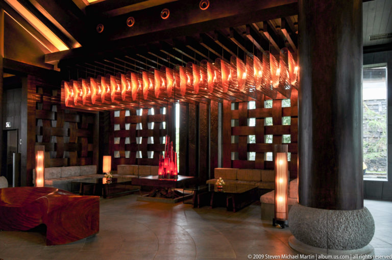 Modern lounge interior in Lijiang, China, with repeated translucent leaf-like ceiling fixtures above dark timber columns and low seating.