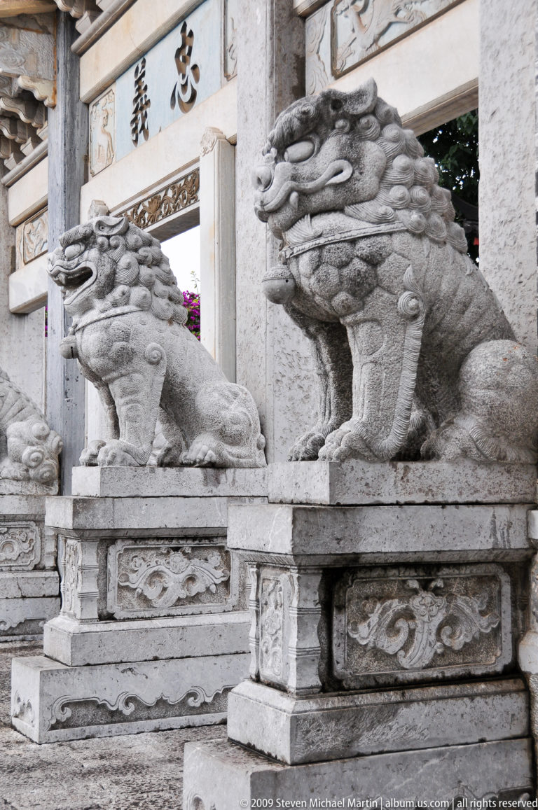 Close-up of lion-like stone guardian statues with scaled bodies, curled manes, and clawed feet on relief-decorated pedestals in Lijiang, Yunnan, China.