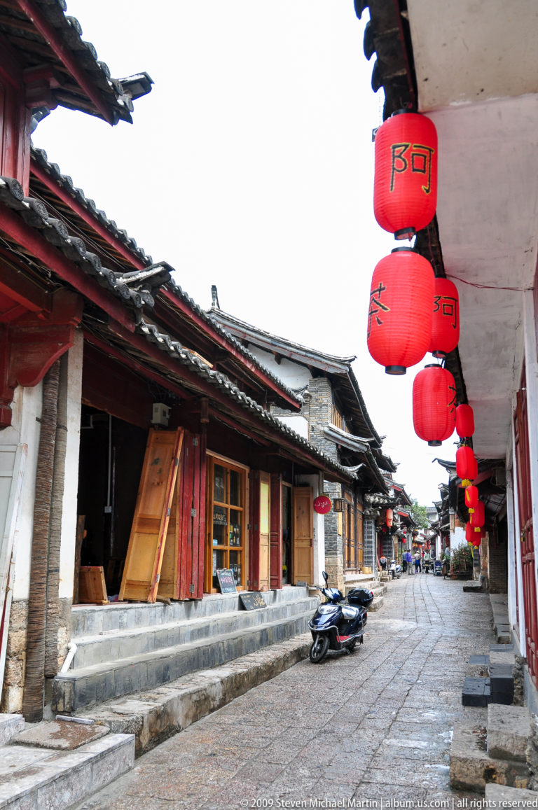 Lantern-lined traditional shopfronts along a stone-paved lane in Lijiang, Yunnan, China.