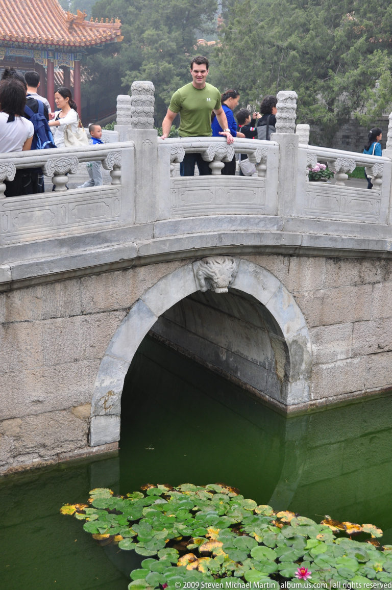 Stone arched bridge with carved balustrades above a green lotus pond at the Summer Palace in Beijing.
