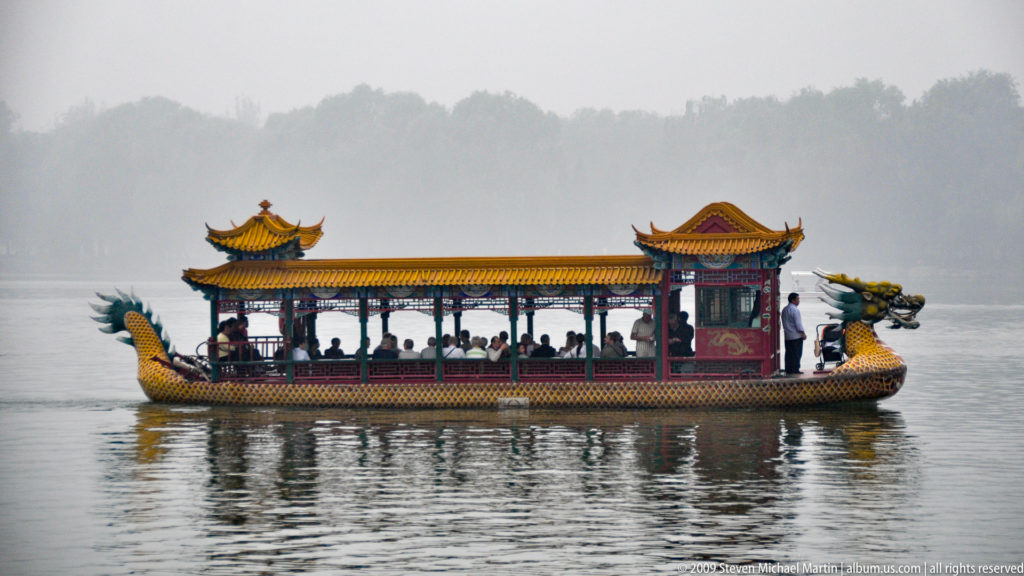 Colorful covered dragon boat with yellow roofs and red columns carrying passengers across hazy Kunming Lake.