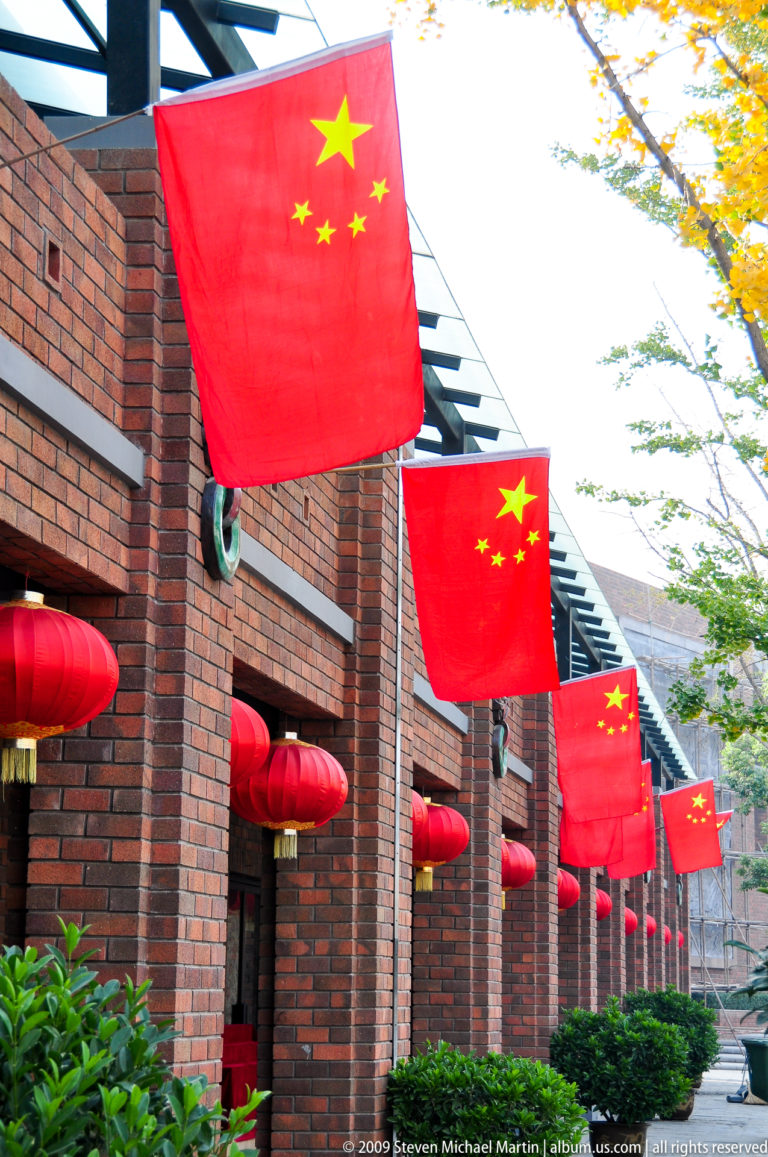 Chinese national flags and red lanterns hanging along the brick facade of a commercial building.