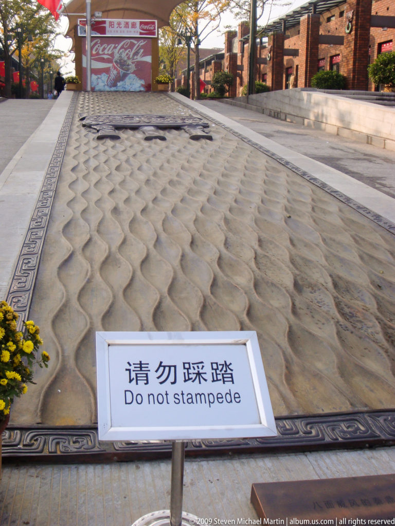 Textured ceremonial pavement with repeating wave-like relief beside a bilingual warning sign at the Mausoleum of the First Qin Emperor near Xi'an.