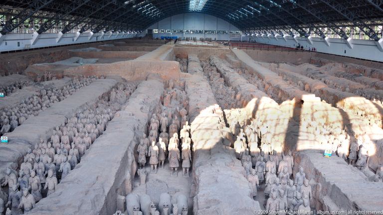 Wide view of Pit 1 showing long earthen trenches filled with rows of standing terracotta warriors inside a large roofed excavation hall.