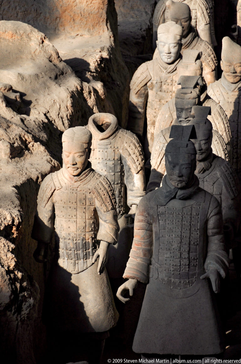 Two terracotta warriors, one sunlit and one in deep shadow, at the Mausoleum of the First Qin Emperor near Xi'an.