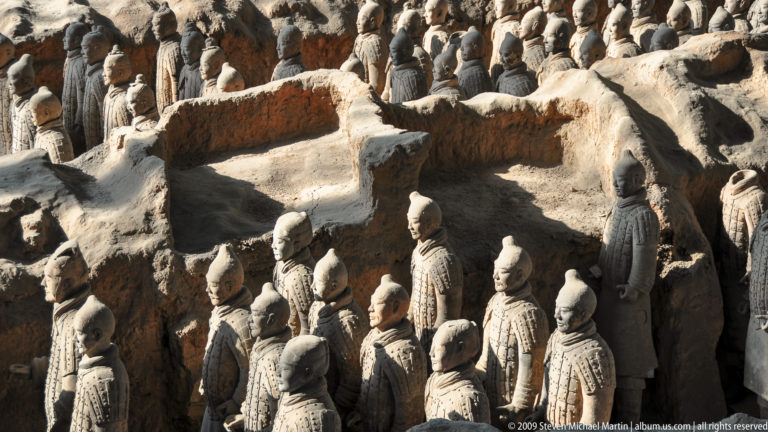 Elevated view of rows of terracotta soldiers standing in parallel trenches separated by earthen walls at the Terracotta Army site near Xi'an.