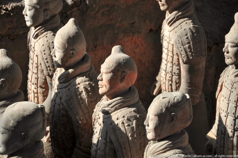 Three-quarter view from above and behind of Qin dynasty terracotta soldiers with topknots and wrapped collars.
