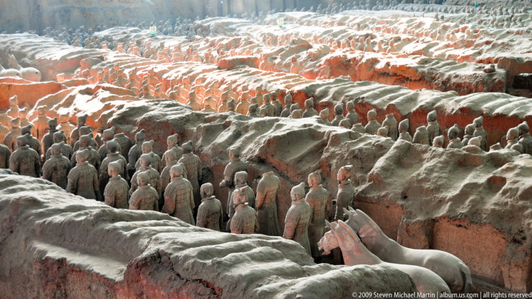 Wide excavation view of terracotta soldiers and horse figures arranged in rows along earthen ridges at the Terracotta Army site near Xi'an.