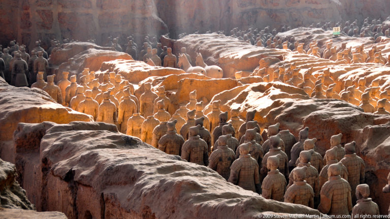 Wide sunlit view of dense terracotta infantry ranks extending deep into the excavation at the Mausoleum of the First Qin Emperor near Xi'an.