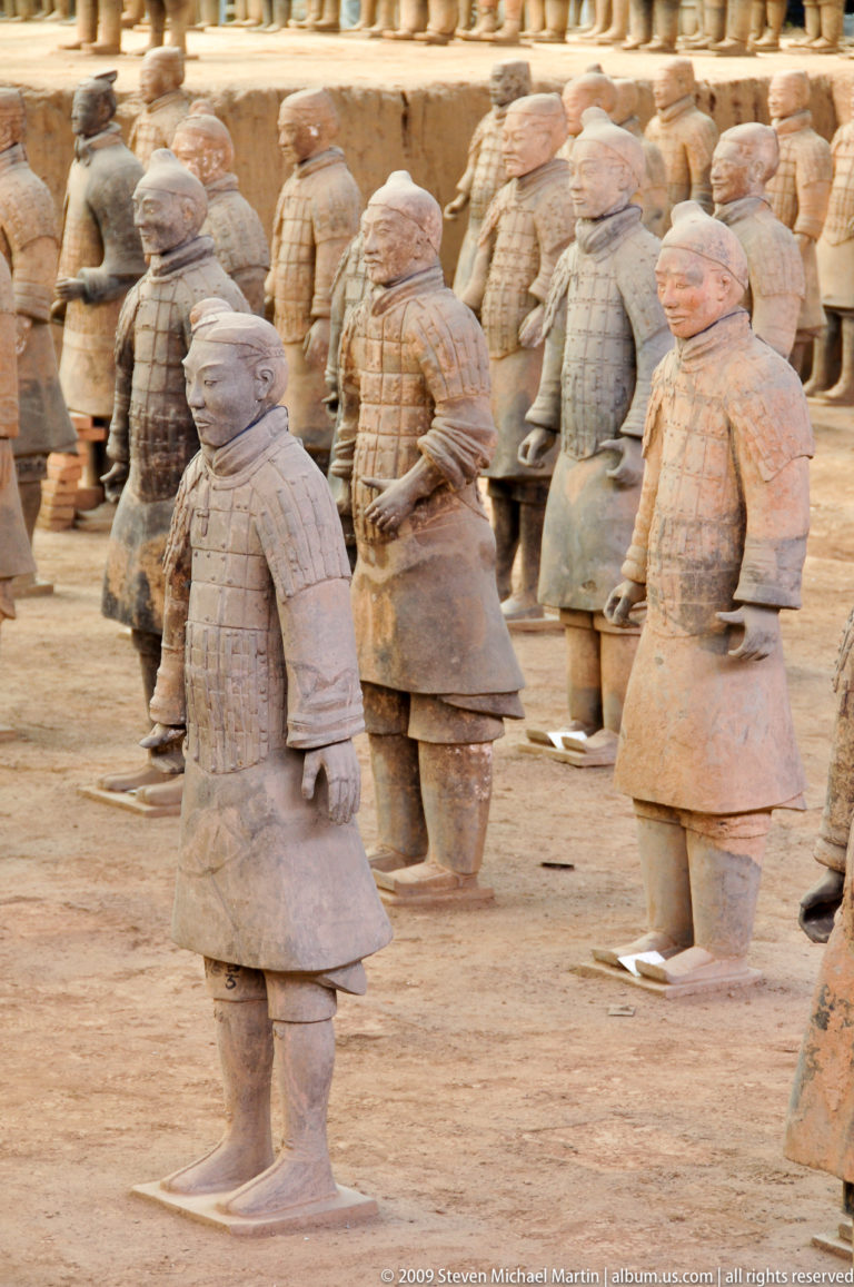 Lower-torso view of standing terracotta warrior figures showing modeled hands and layered garments.