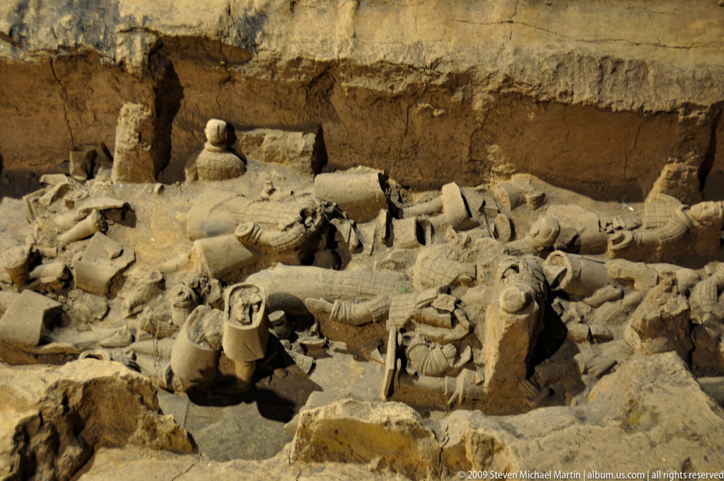 Collapsed terracotta warrior torsos, heads, and fragments lying across the crowded floor of an excavation pit.