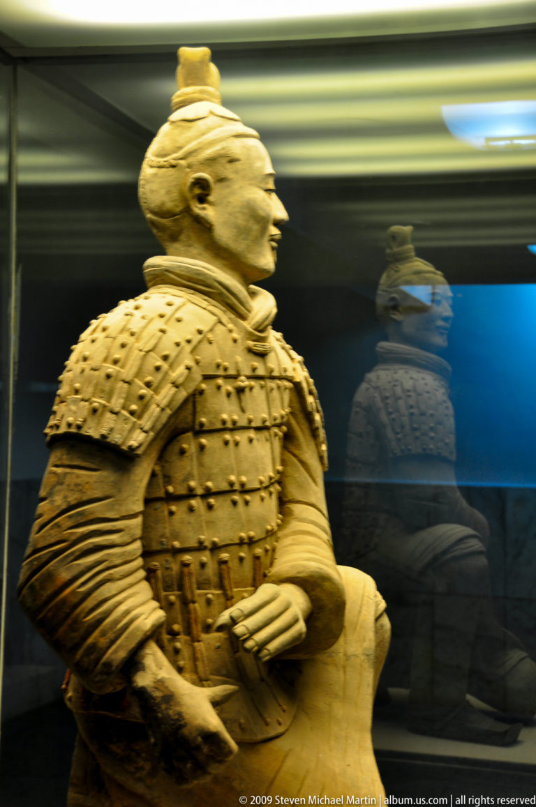 Close view of a terracotta warrior’s studded armored torso reflected in the glass of a museum case.