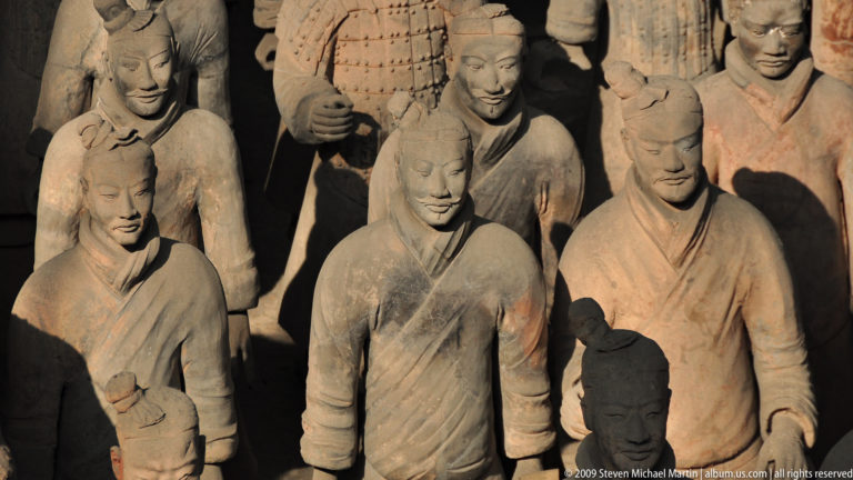 Close group of unarmored, robed terracotta infantry figures standing in formation with armored soldiers visible behind them.