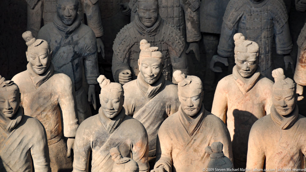 Overhead view of robed, unarmored terracotta infantry standing in front of darker armored soldiers.