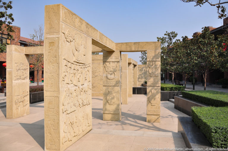 Modern stone panels with historical-style relief carvings forming an outdoor passage at the Terracotta Army museum complex near Xi'an.