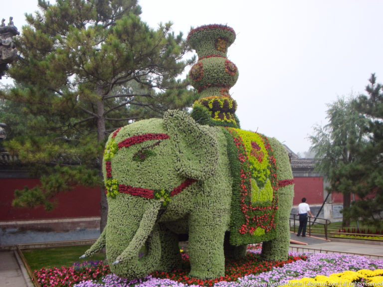 Life-sized elephant-shaped floral topiary with red and yellow decorative patterns on its body.