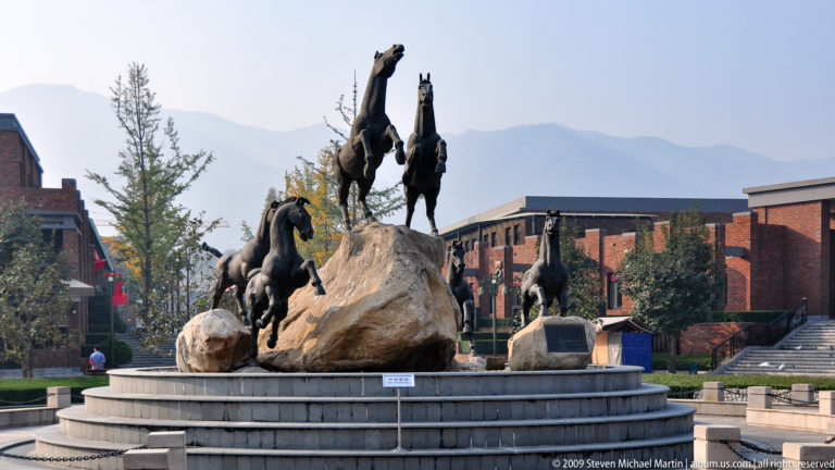 Modern monumental outdoor sculpture of several galloping horses arranged around a central rock-like mass at the Terracotta Army museum complex near Xi’an.