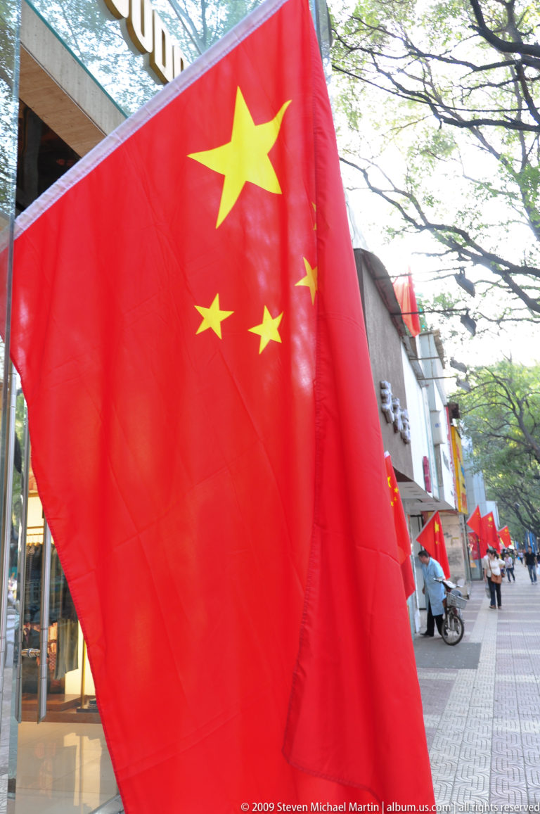 Large Chinese national flag in the foreground with a row of similar red flags lining a tree-lined sidewalk in Xi’an.