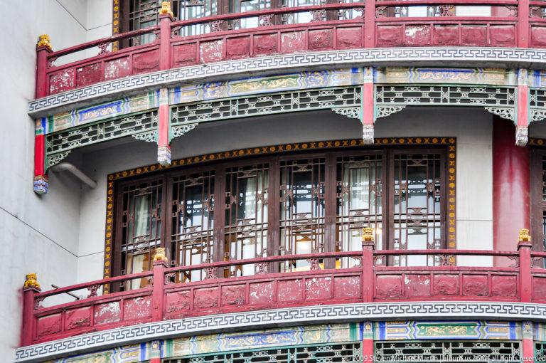 Curved red balconies with lattice windows and painted Chinese ornament on the corner of a multi-story commercial building.