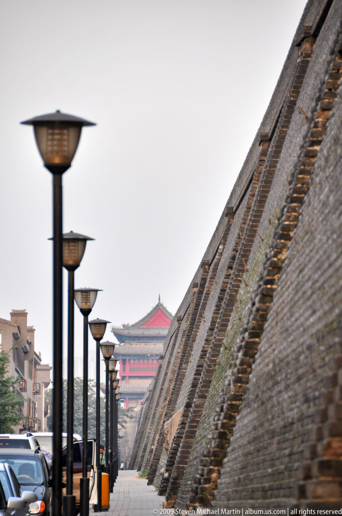 Long brick rampart of the Xi’an City Wall receding toward a red-roofed gate tower lined with street lamps.