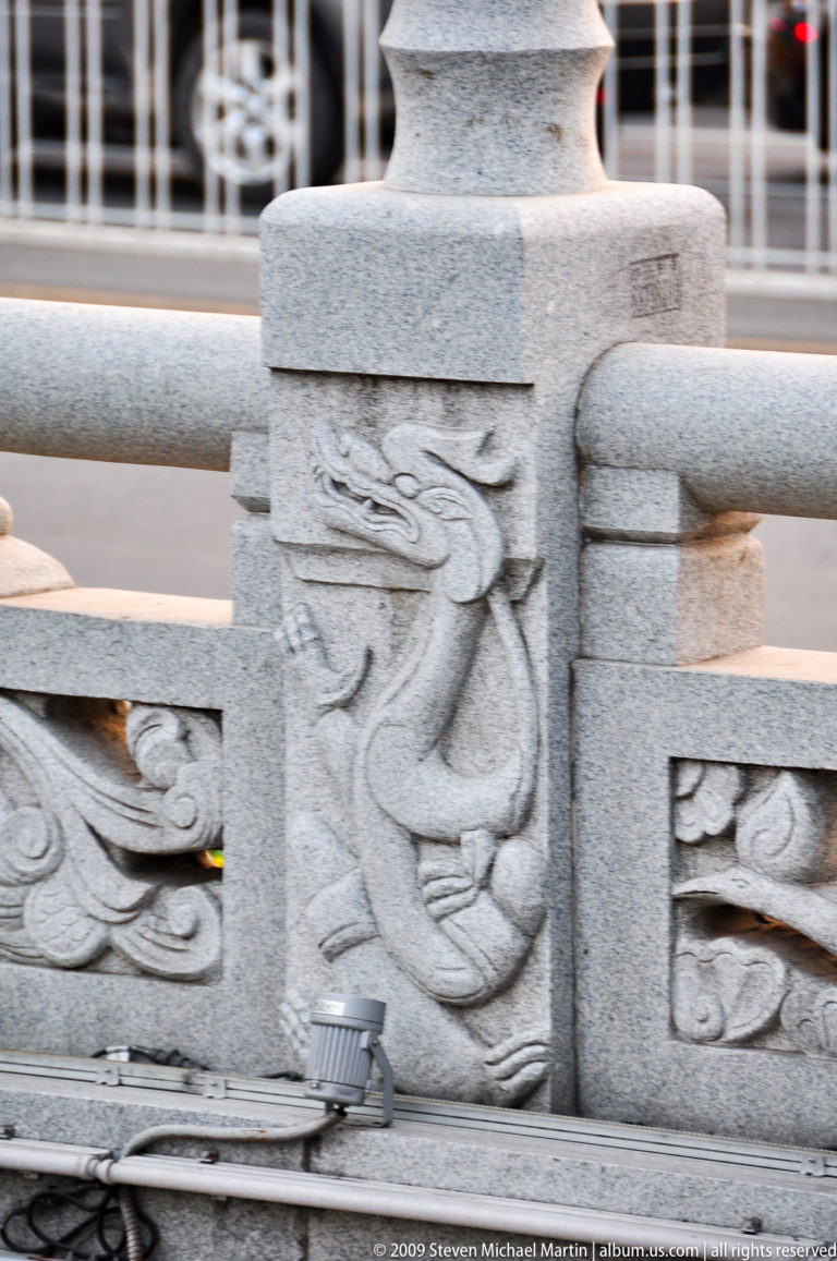 Shallow relief carving of a sinuous Chinese dragon on a pale stone balustrade panel in Xi’an.
