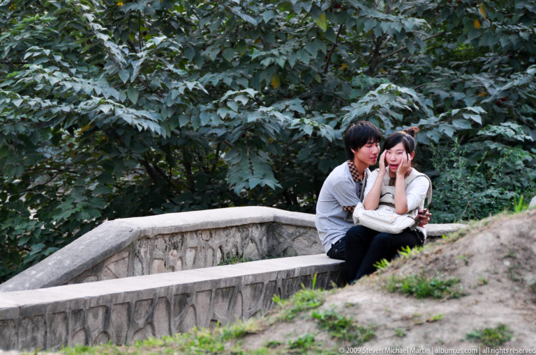 Young couple sitting close together beside a carved stone railing in a leafy Xi’an park.