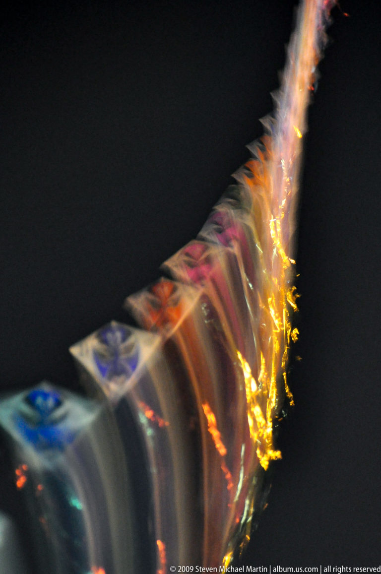 Curved line of repeated diamond-shaped forms with a bright golden light trail, blurred by long exposure at night.