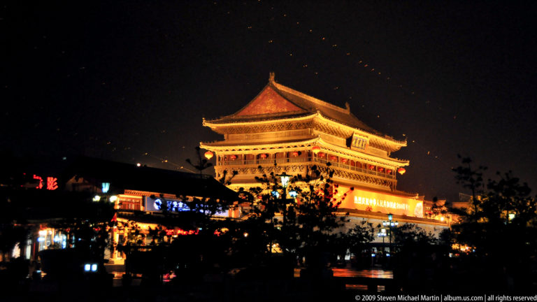 Illuminated Drum Tower of Xi’an at night, with its lower platform partly hidden by trees and festive street lights.
