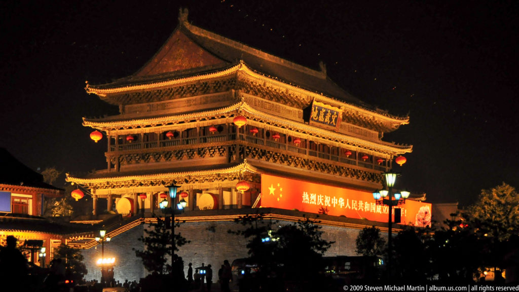 Illuminated Drum Tower of Xi’an at night, with red lanterns and a large National Day banner on its high masonry base.