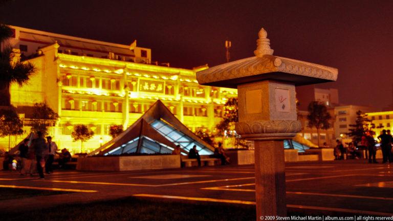 Carved stone street fixture beside a low glass pyramid skylight in an illuminated Xi’an plaza.