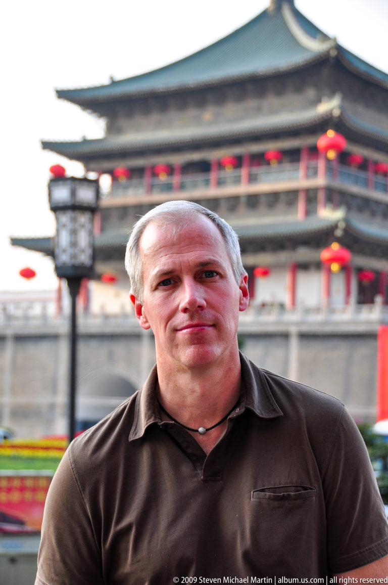 Close portrait of a male traveler facing the camera with the Xi’an Bell Tower blurred in the background.