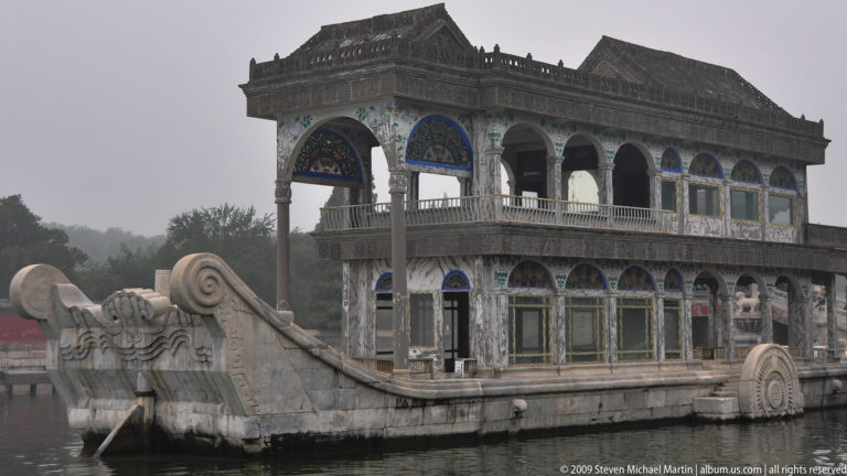Marble Boat at the Summer Palace, with a stone hull, two-story pavilion, arched windows, and decorative wheel forms beside Kunming Lake.