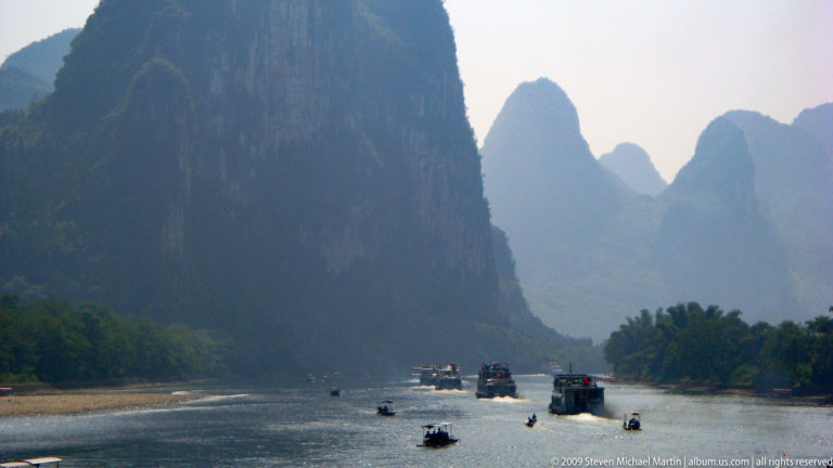 Tour boats travel along the Li River between towering, hazy karst cliffs.