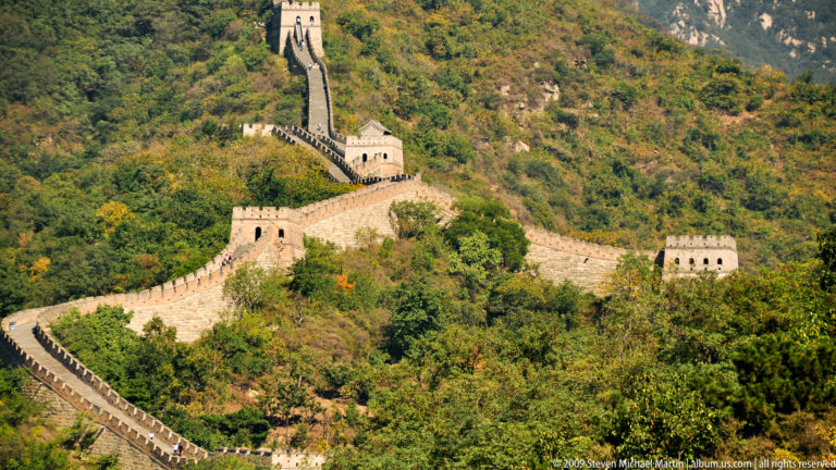 Telephoto view of the Great Wall at Mutianyu, with multiple Ming-dynasty watchtowers and ramparts zigzagging along an autumn mountainside.