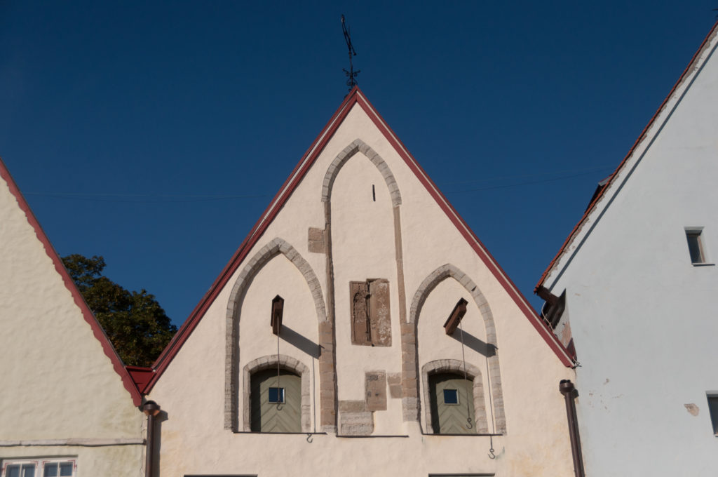 Small steep gable with paired pointed openings and dark stone trim on the pale exterior of St Nicholas Church.