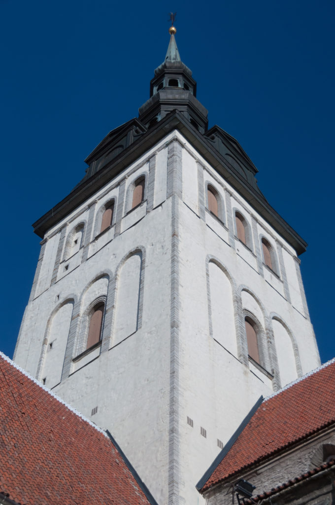 Low-angle view of the broad white tower of St Nicholas Church rising above red tile roofs beneath a dark lantern roof.