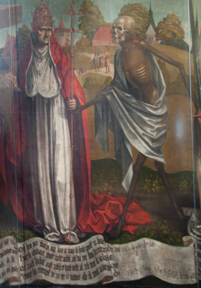 Clerical figure with a cross-staff beside a skeleton in the Dance of Death, above a scrolling band of Low German verse.