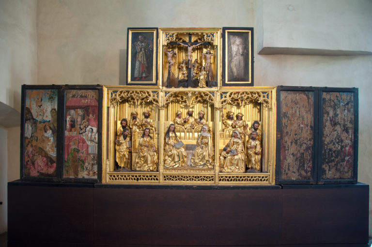 Open winged altarpiece with gilded carved figures, Gothic tracery, painted side panels, and a smaller sculptural upper register.