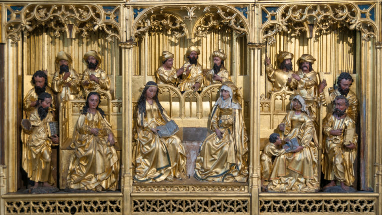 Three gilded carved narrative groups beneath ornate Gothic tracery in the lower register of a medieval altarpiece.