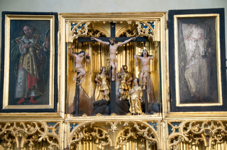 Carved Crucifixion group with Christ and two thieves, surrounded by gilded Gothic tracery and flanked by painted panels.
