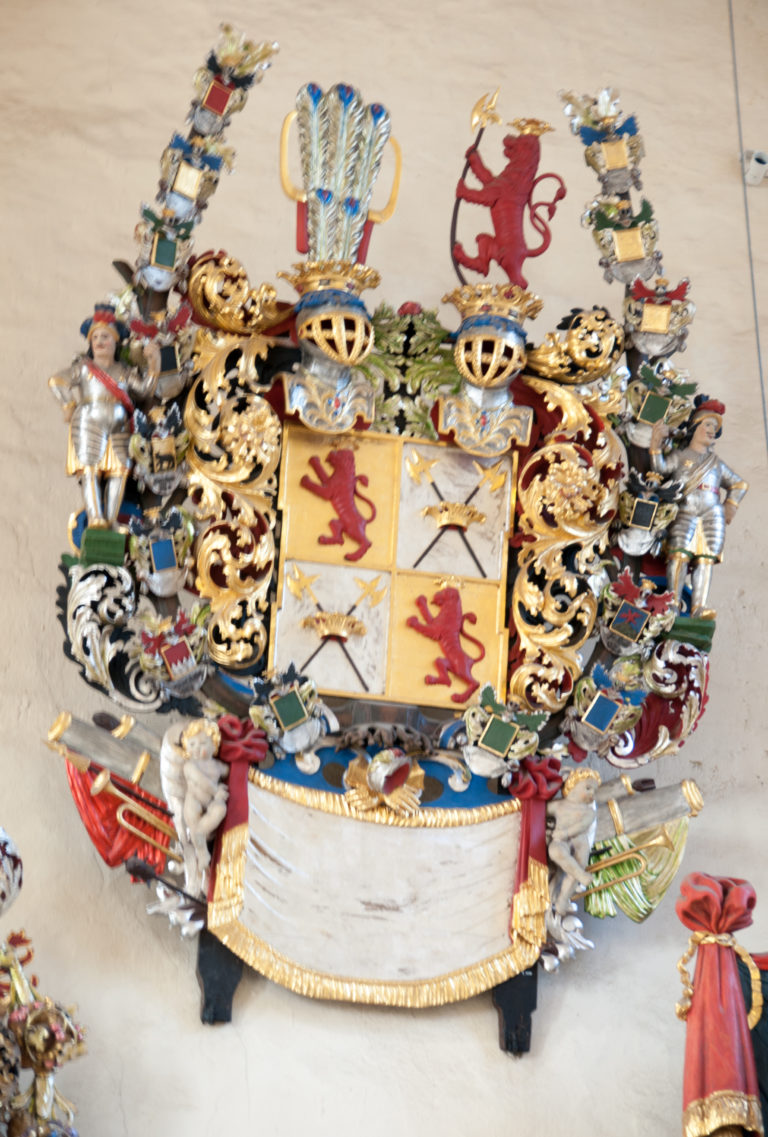 Large ornate coat of arms with quartered shield, crowned helmet, curling mantling, lions, and numerous surrounding heraldic devices.