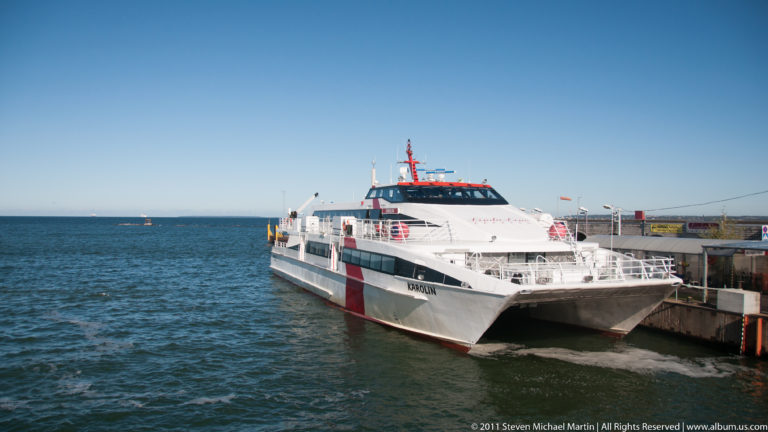 White fast catamaran Karolin docked at Tallinn harbor, with twin bows, red hull stripes, and passenger cabin visible.