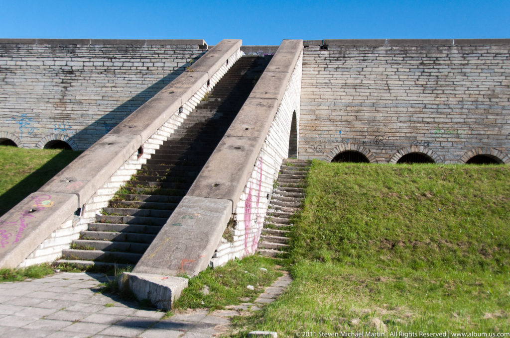 Broad concrete stairway climbing the grass-covered terraces and low arched walls of Tallinn Linnahall.
