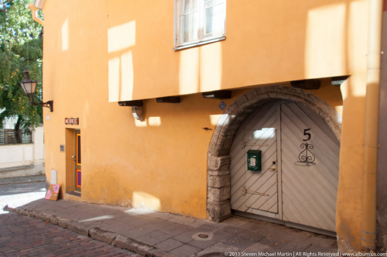 Gray wooden doorway marked 5 within a broad stone arch on an ochre historic façade in Tallinn.
