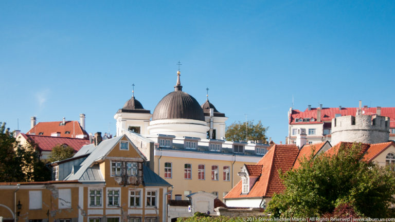 Elevated Tallinn Old Town view with a dark dome, pastel façades, red roofs, and a small stone tower.