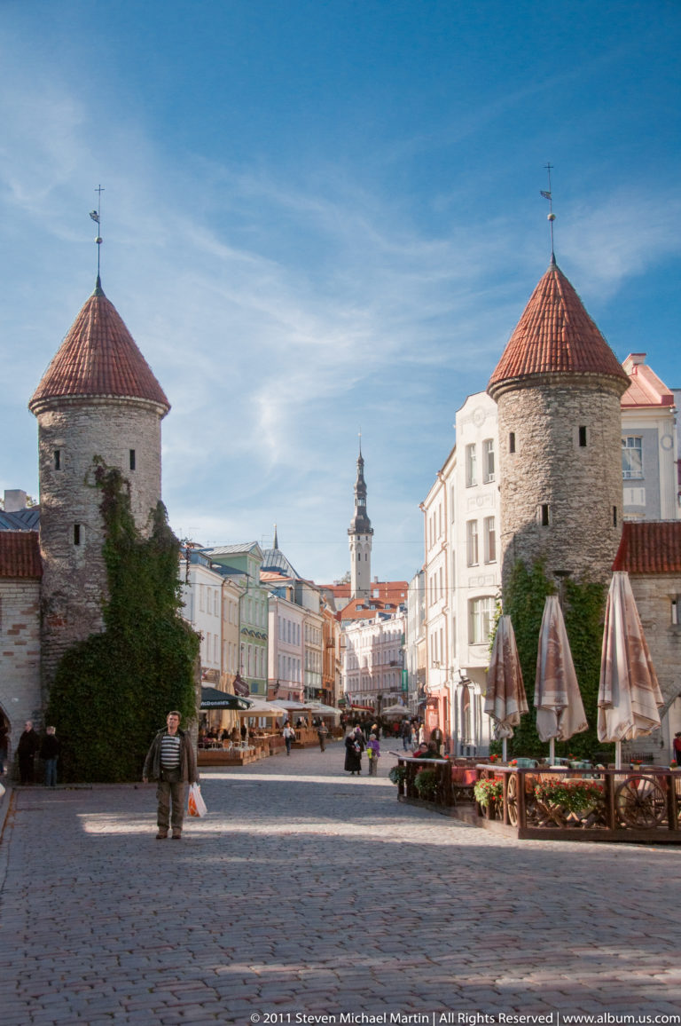 Two round stone towers of Viru Gate with red conical roofs framing a cobbled entrance into Tallinn Old Town.